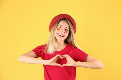 Portrait of pretty woman making heart with her hands on color background