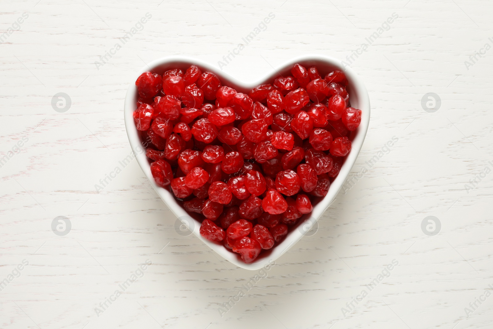 Photo of Heart shaped bowl of sweet cherries on wooden background, top view. Dried fruit as healthy snack