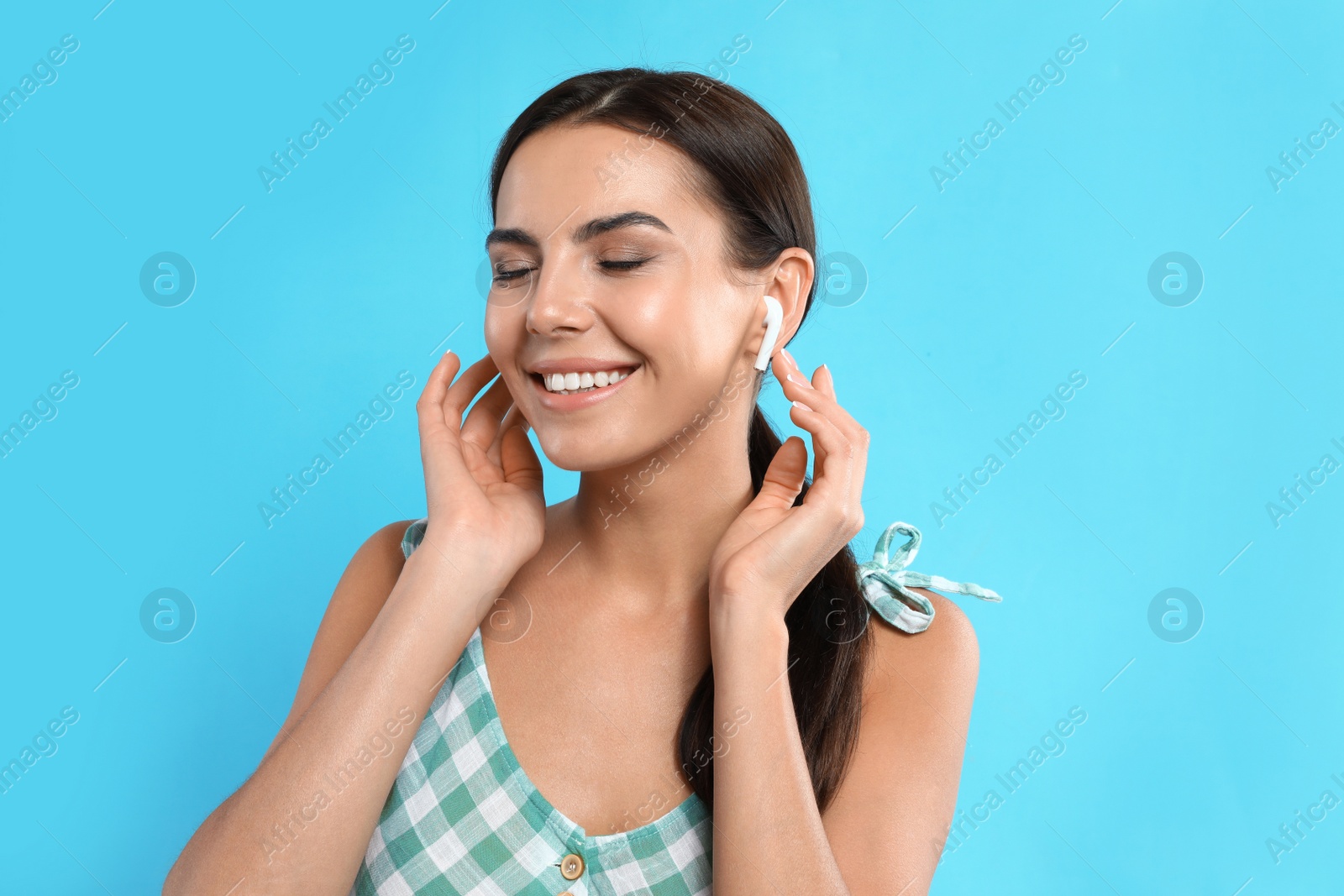 Photo of Happy young woman listening to music through wireless earphones on light blue background