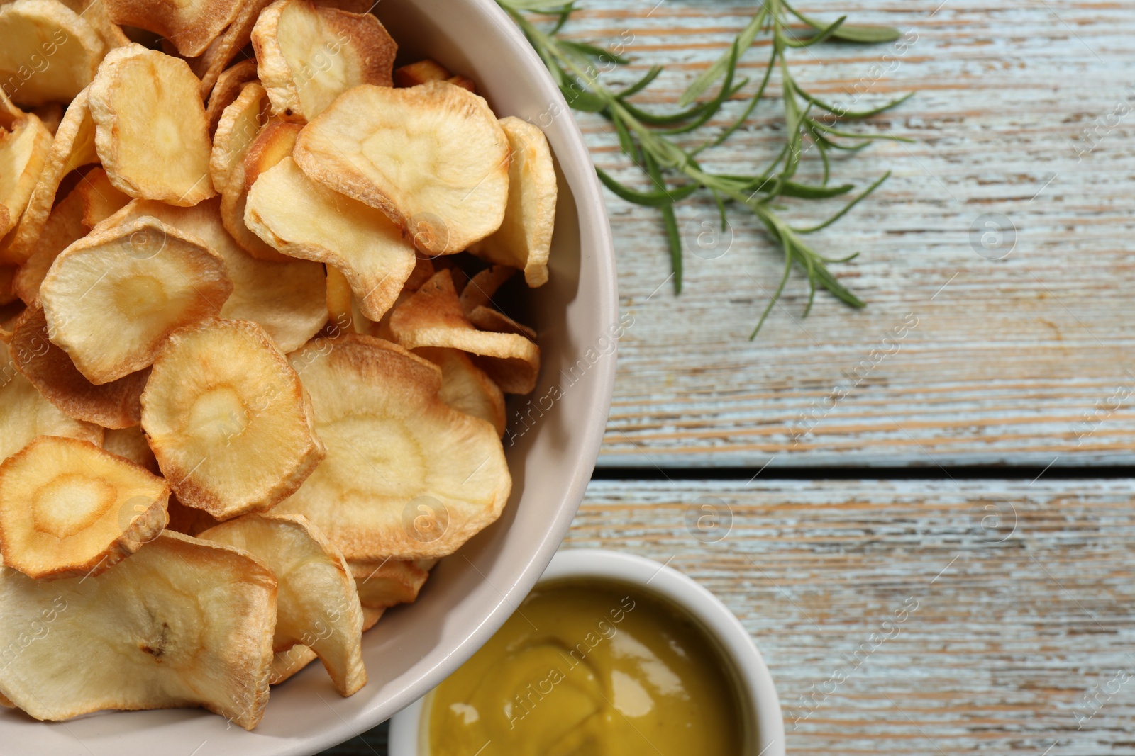 Photo of Tasty homemade parsnip chips with sauce and rosemary on old light blue wooden table, flat lay. Space for text