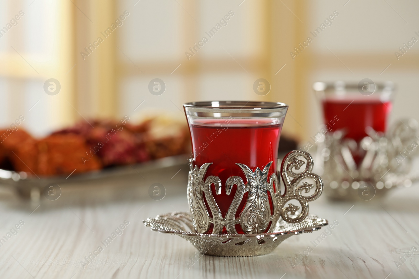 Photo of Glass of traditional Turkish tea in vintage holder on white wooden table