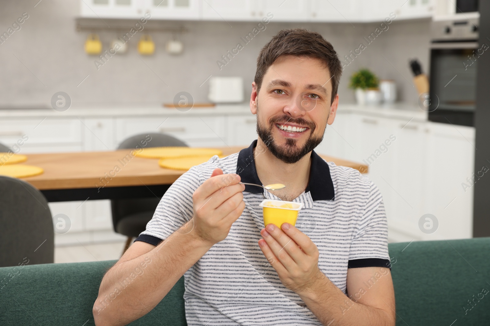 Photo of Handsome man with tasty yogurt on sofa in kitchen