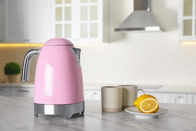 Modern electric kettle, cups and lemons on table in kitchen