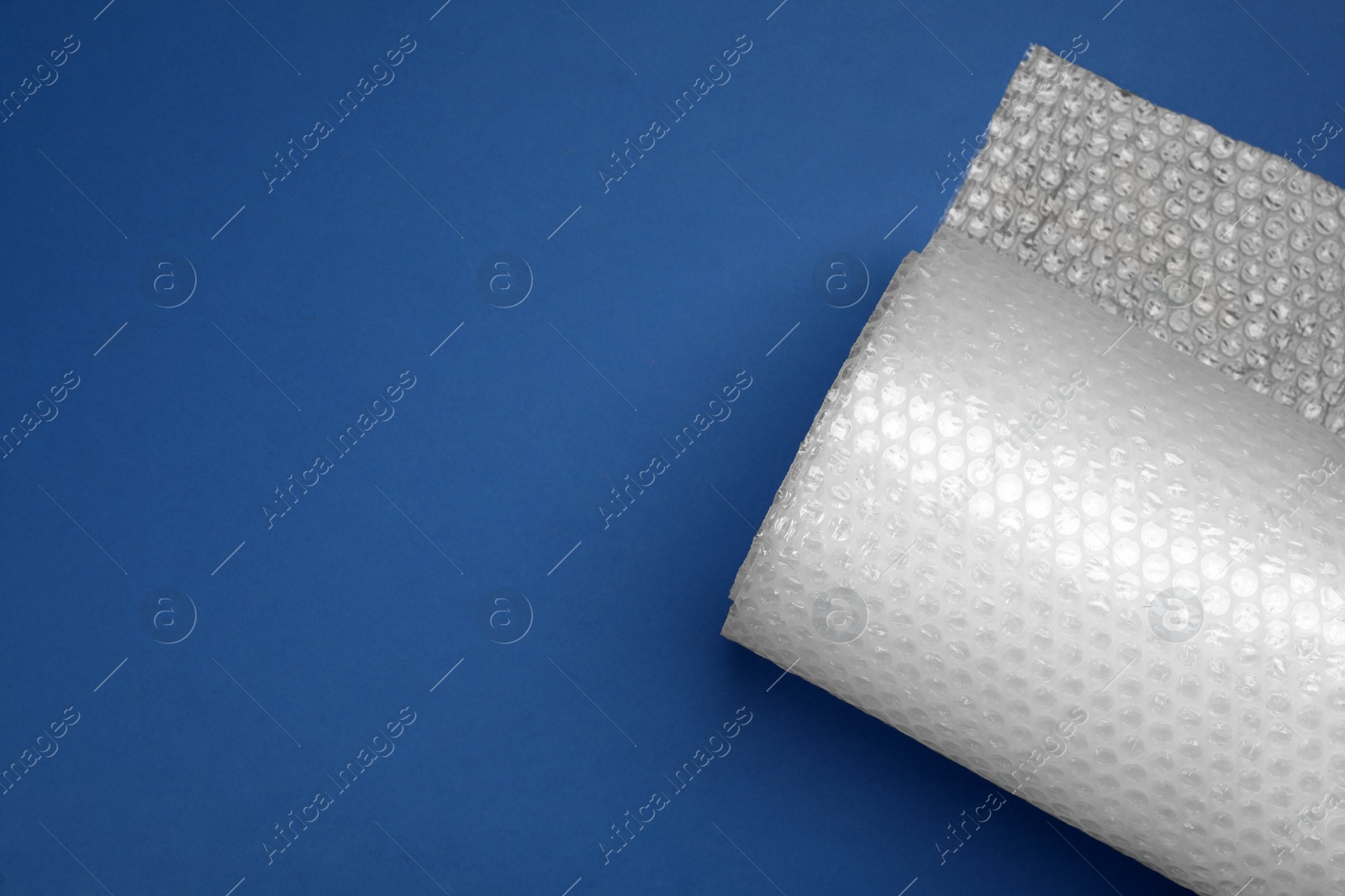 Photo of Bubble wrap roll on blue background, top view. Space for text