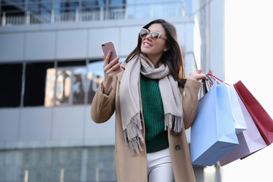 Photo of Beautiful young woman with shopping bags and smartphone outdoors