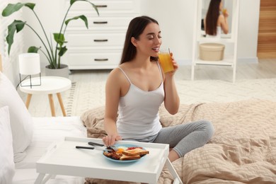 Photo of Happy young woman having breakfast on bed at home