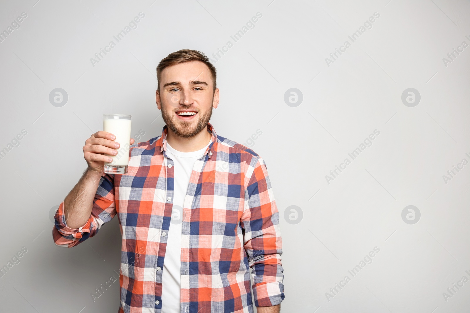 Photo of Young man with glass of tasty milk on light background