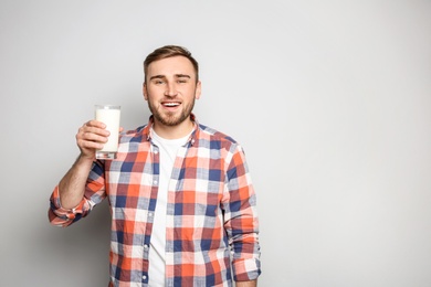 Young man with glass of tasty milk on light background