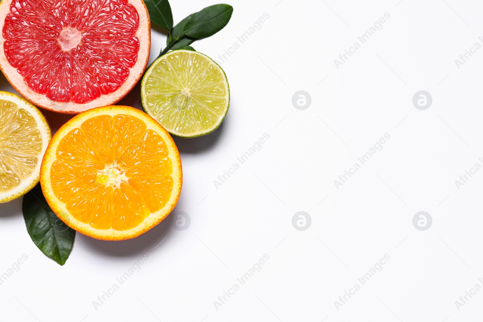 Photo of Different cut citrus fruits and leaves on white table, flat lay. Space for text