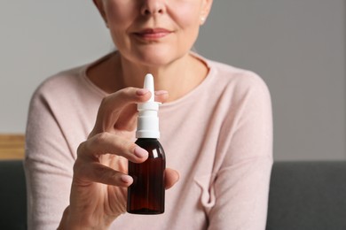 Woman holding nasal spray indoors, focus on bottle