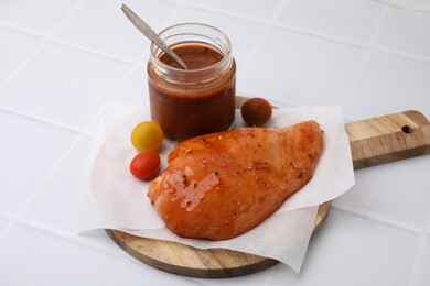 Photo of Fresh marinade and raw chicken fillets on white tiled table