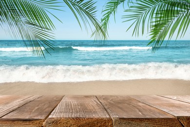 Image of Wooden table under green palm leaves on beach near ocean