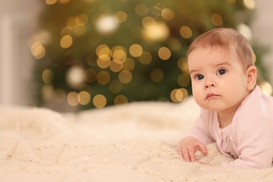 Photo of Portrait of cute little baby on knitted blanket against blurred festive lights, space for text. Winter holiday