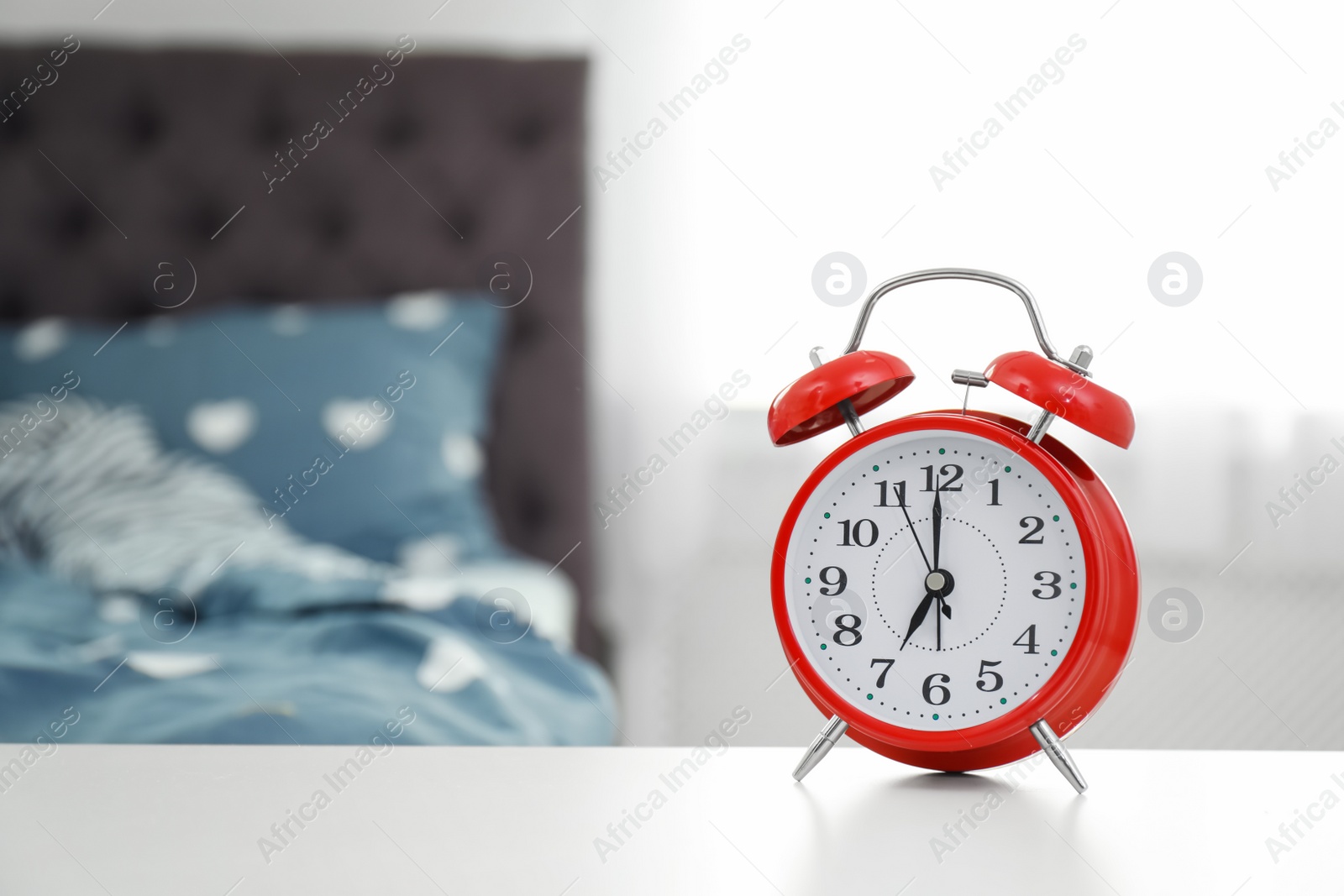 Photo of Analog alarm clock on table in bedroom. Time of day