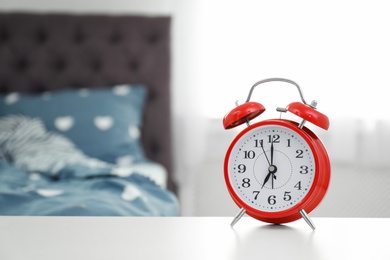 Photo of Analog alarm clock on table in bedroom. Time of day