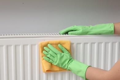 Photo of Woman cleaning radiator with rag indoors, closeup