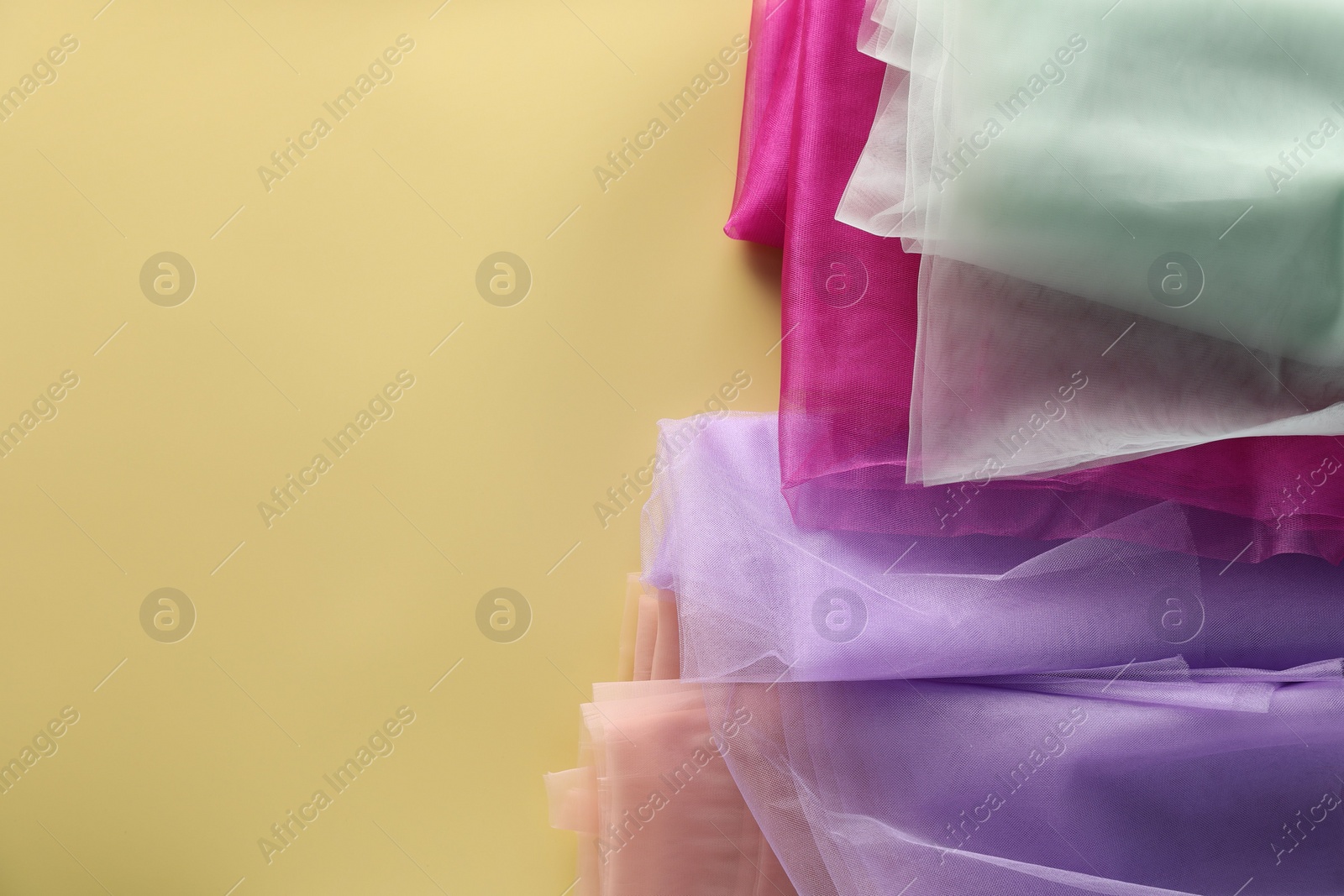 Photo of Beautiful tulle fabrics on yellow background, flat lay. Space for text