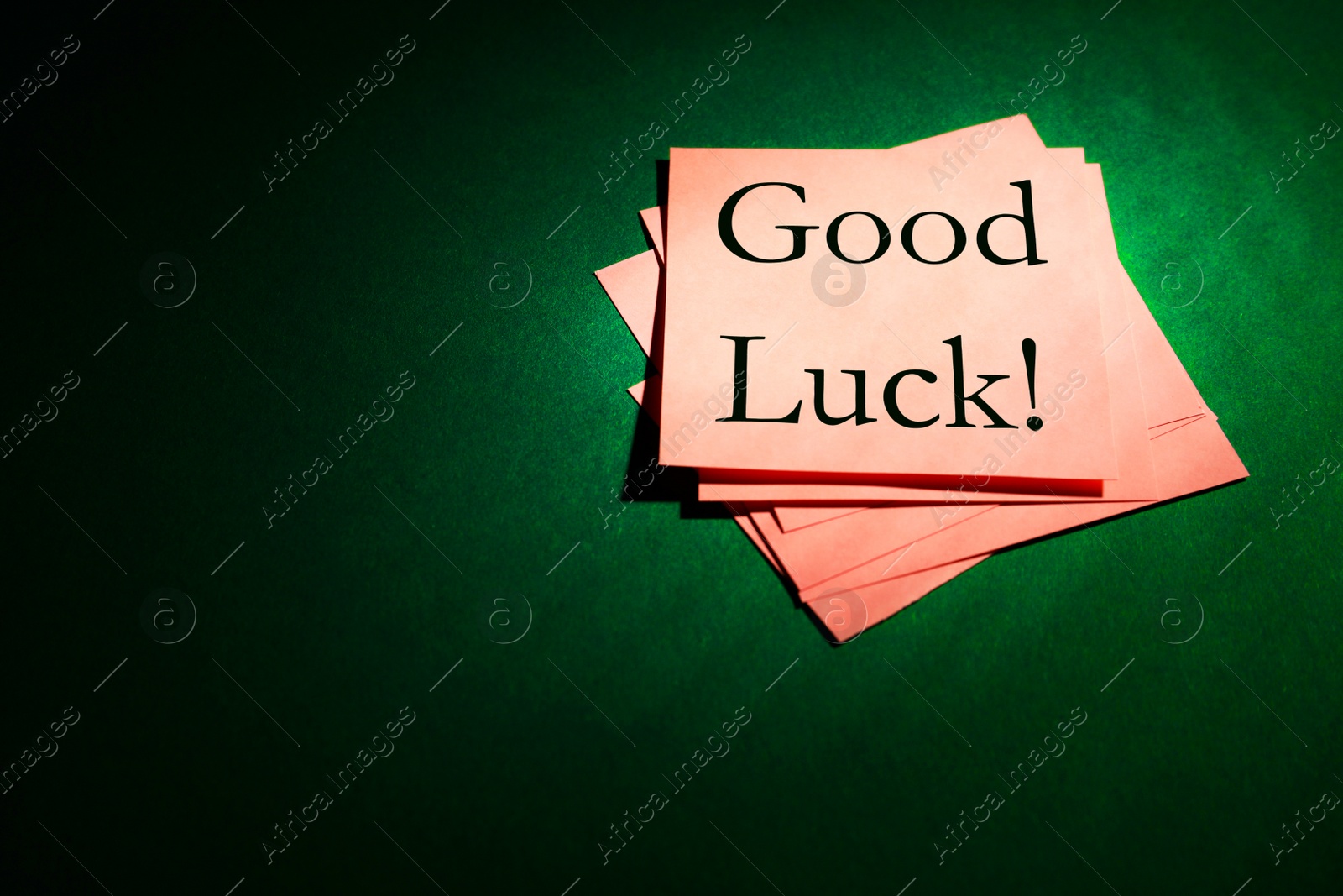 Image of Pink notes with phrase GOOD LUCK on dark green background, above view. Space for text