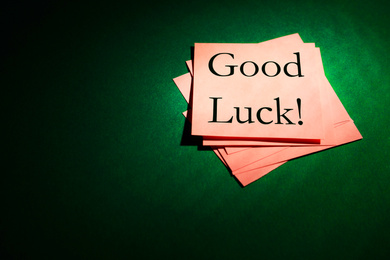 Image of Pink notes with phrase GOOD LUCK on dark green background, above view. Space for text