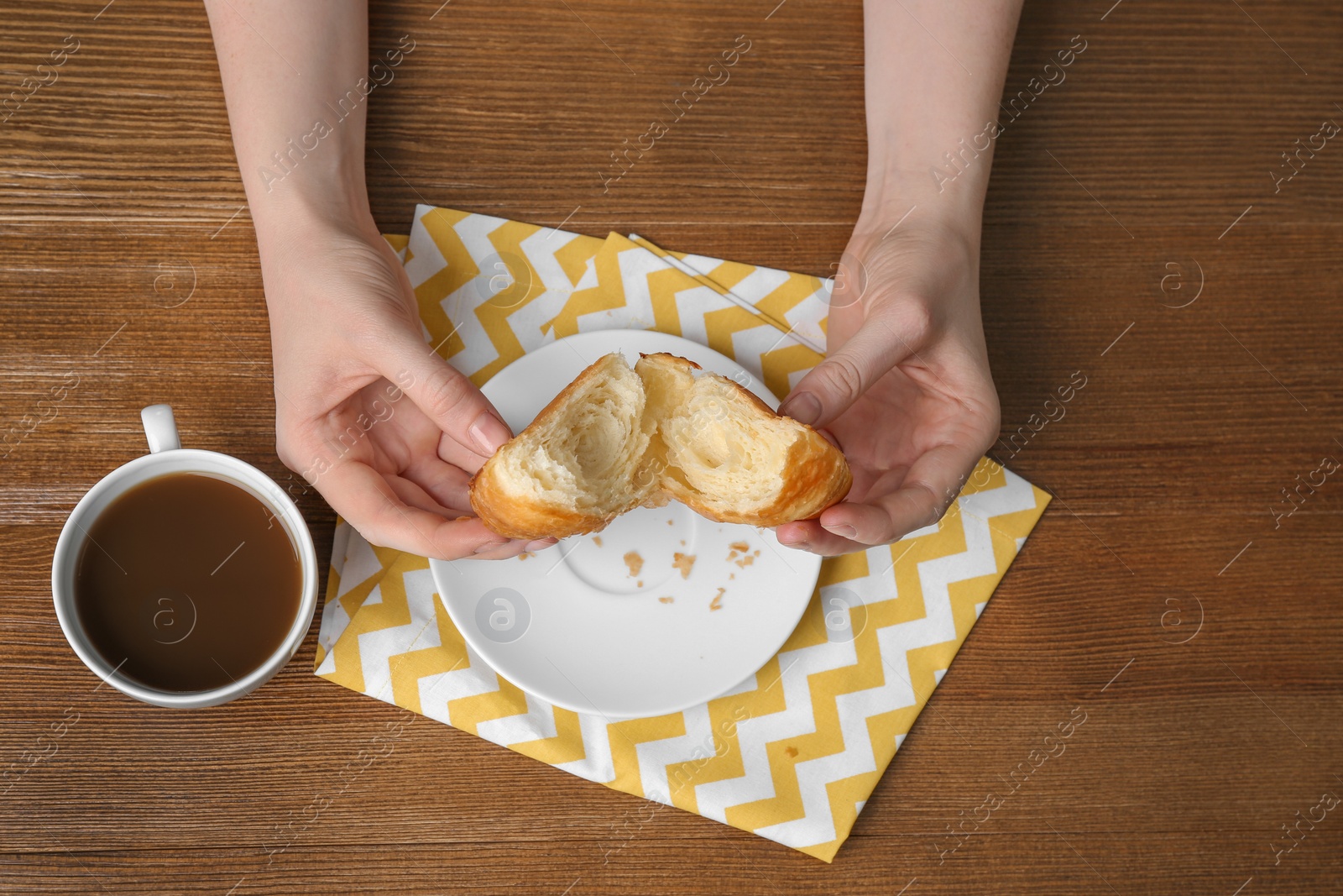 Photo of Young woman having breakfast with tasty croissant and cup of coffee at table, top view