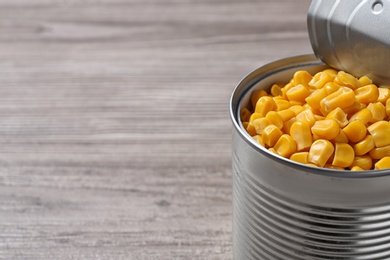 Photo of Open tin can of corn kernels on wooden table. Space for text