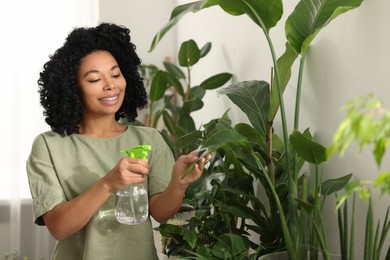 Photo of Happy woman spraying beautiful houseplants with water indoors
