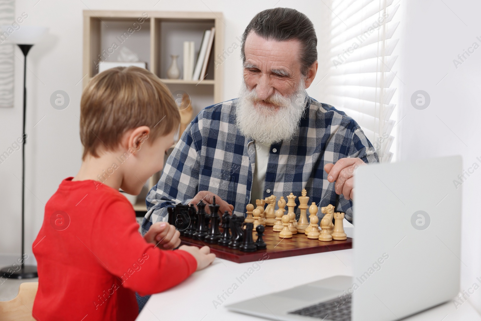 Photo of Grandfather and grandson playing chess following online lesson in room