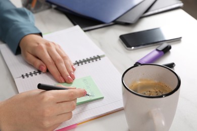 Photo of Woman writing on sticky note at white marble table, closeup