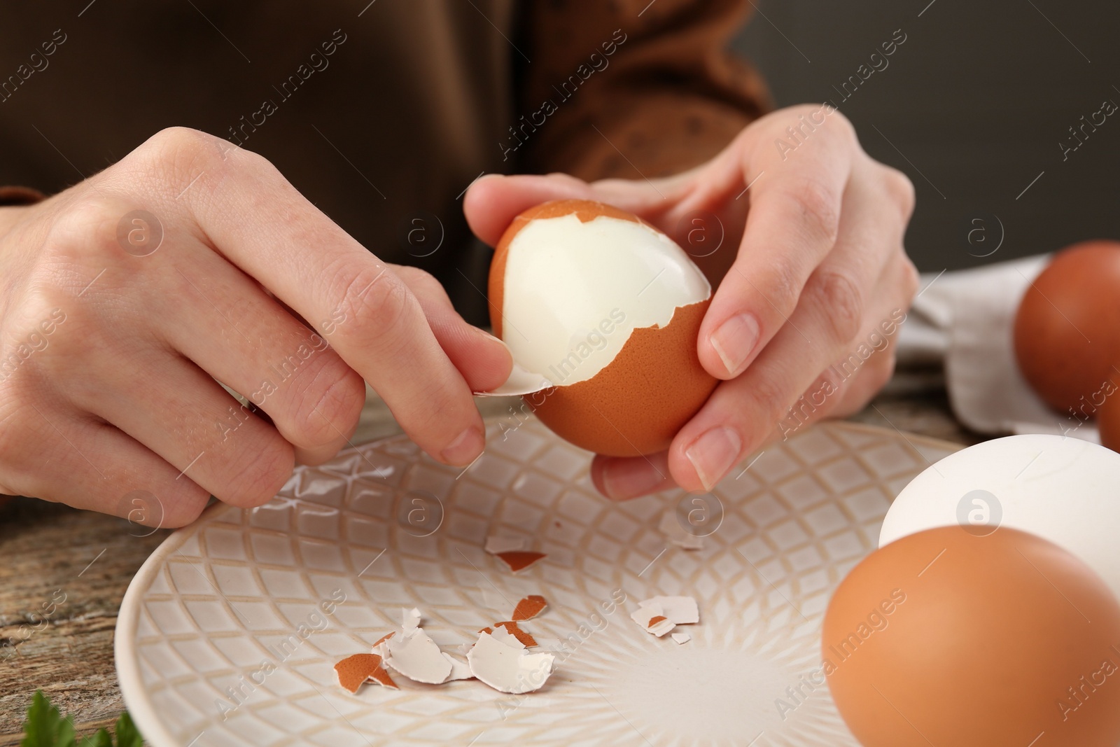 Photo of Woman peeling boiled egg at wooden table, closeup