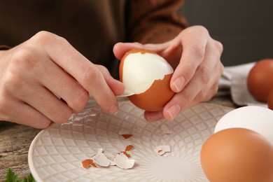 Woman peeling boiled egg at wooden table, closeup