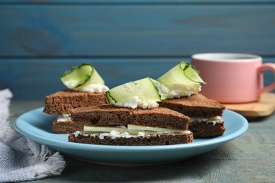 Plate of tasty sandwiches with cucumber and cream cheese on light blue wooden table