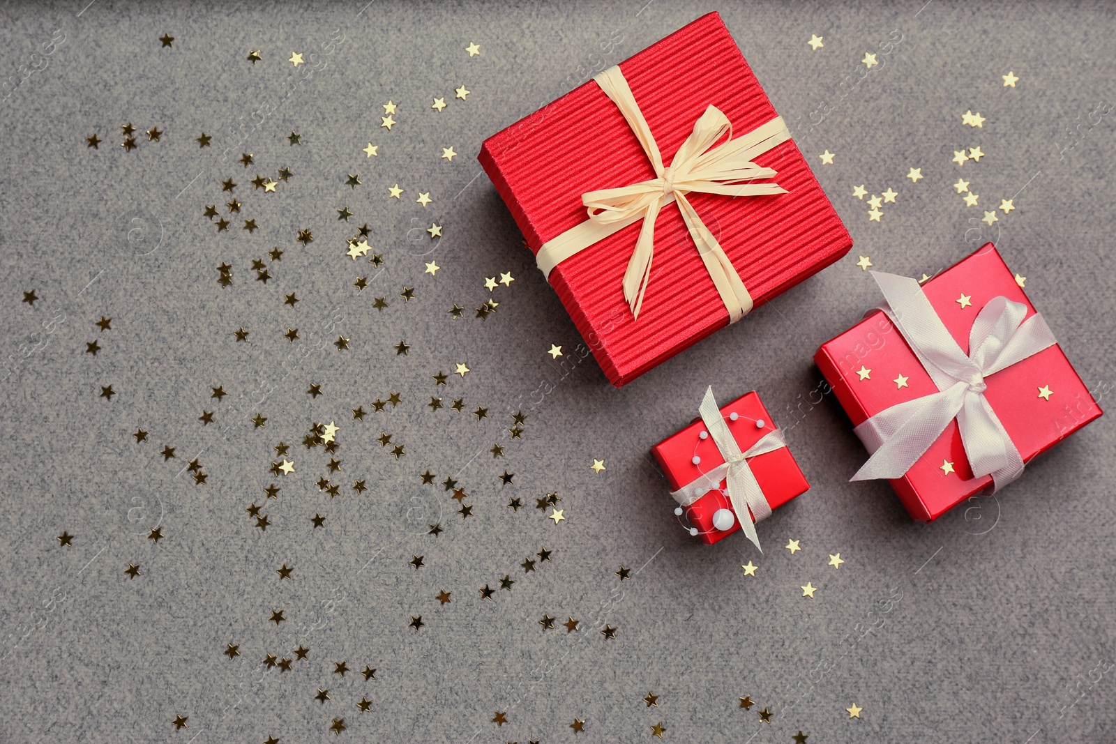 Photo of Christmas gift boxes and shiny confetti on grey background, flat lay. Space for text