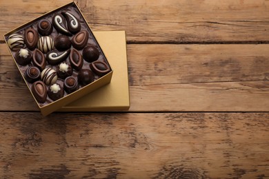 Open box of delicious chocolate candies on wooden table, top view