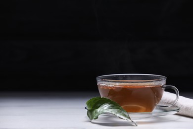 Aromatic hot tea in glass cup and leaf on white table against black background. Space for text