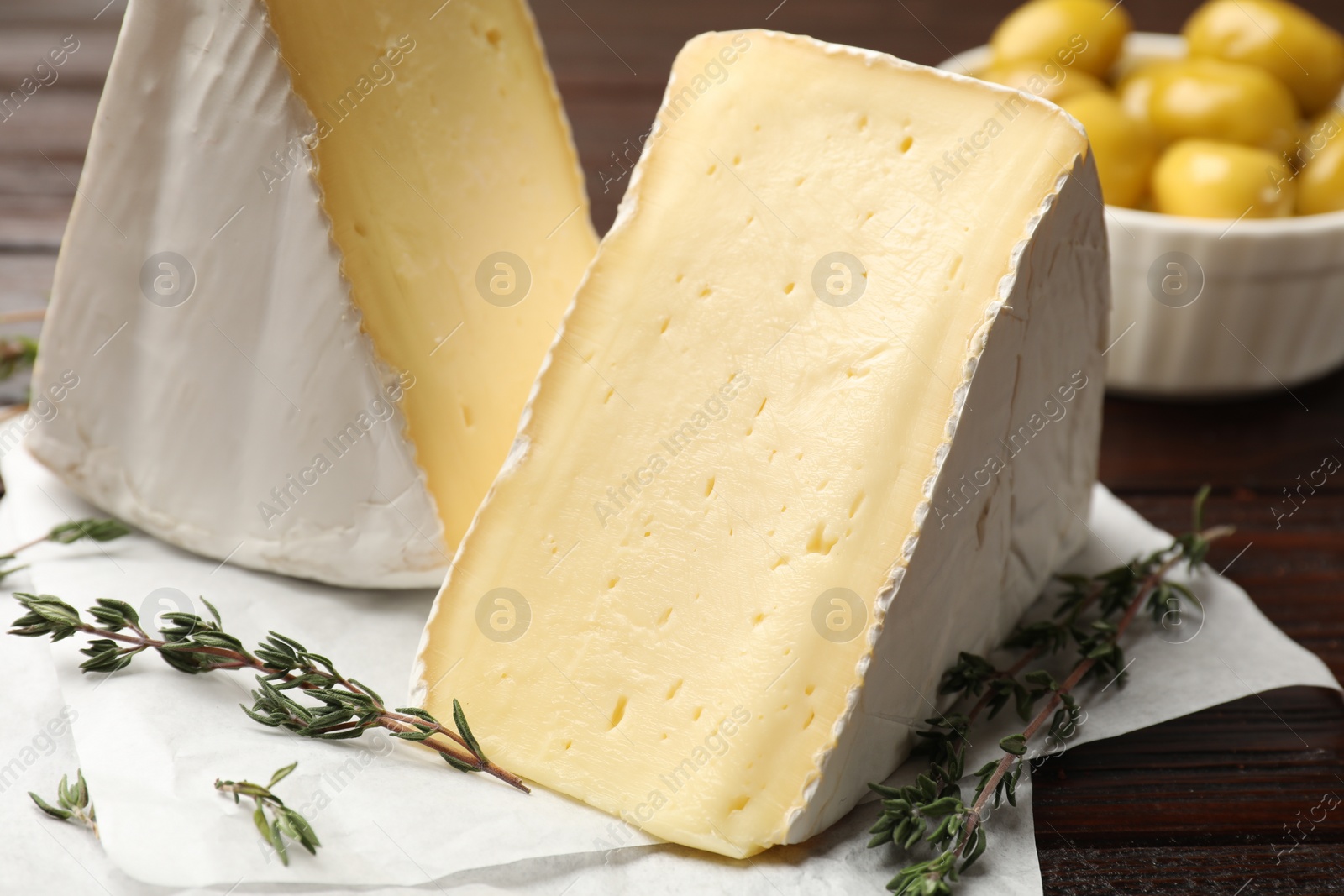 Photo of Pieces of tasty camembert cheese and thyme on wooden table, closeup