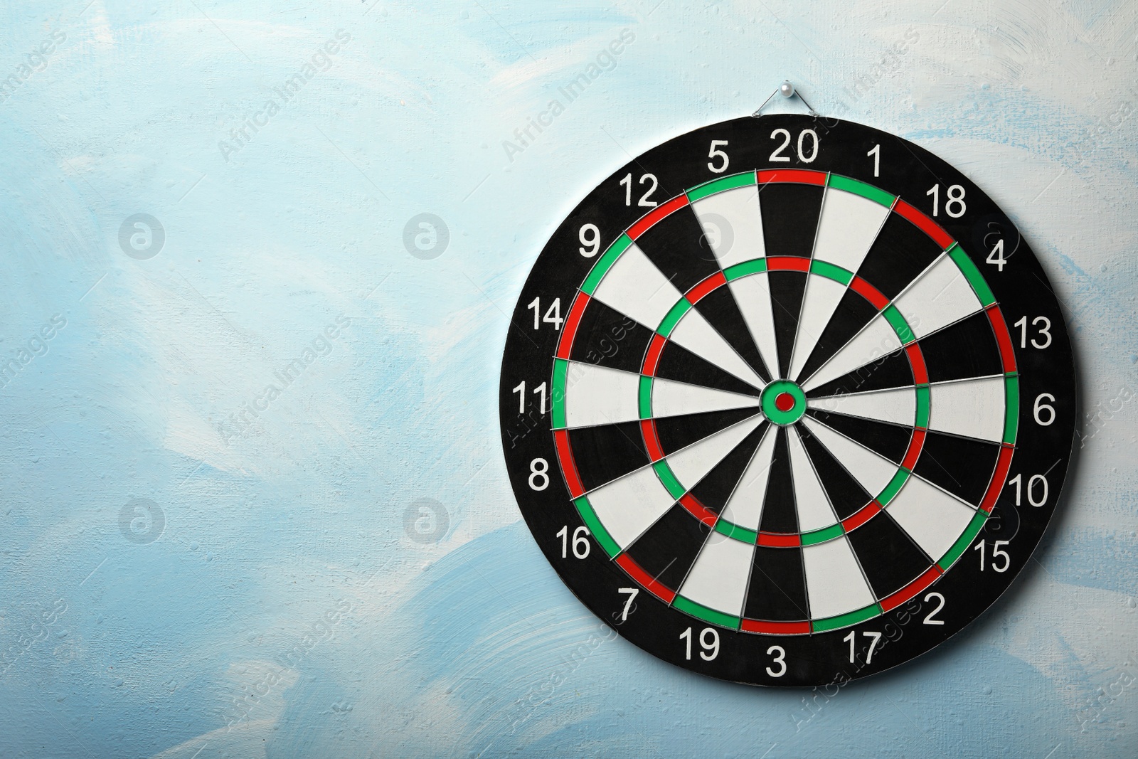 Photo of Dart board hanging on light blue wall. Space for text