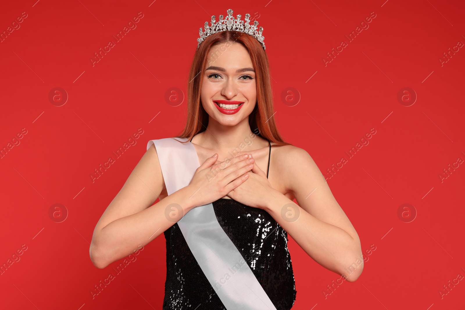 Photo of Beautiful young woman with tiara and ribbon in dress on red background. Beauty contest