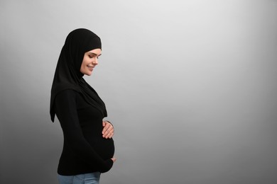 Portrait of pregnant Muslim woman in hijab on light gray background, space for text