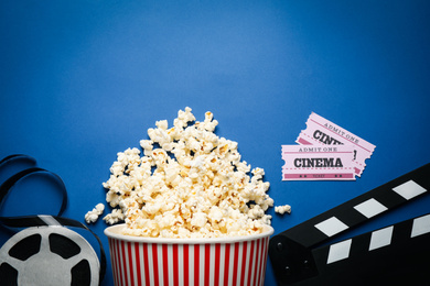 Photo of Flat lay composition with delicious popcorn and cinema items on blue background