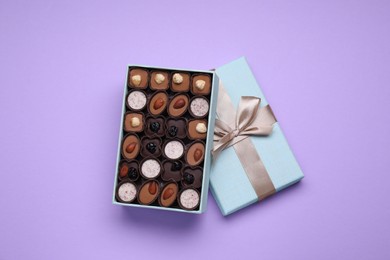Photo of Open box of delicious chocolate candies on violet background, top view