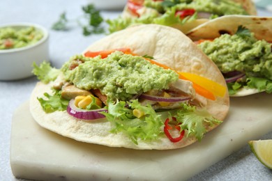 Delicious tacos with guacamole, meat and vegetables on table, closeup