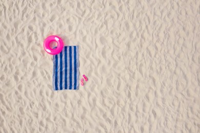 Striped beach towel, flip flops and swim ring on sand, aerial view. Space for text