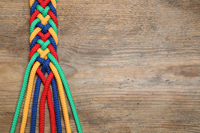Top view of braided colorful ropes on wooden background, space for text. Unity concept