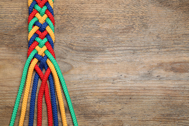 Photo of Top view of braided colorful ropes on wooden background, space for text. Unity concept