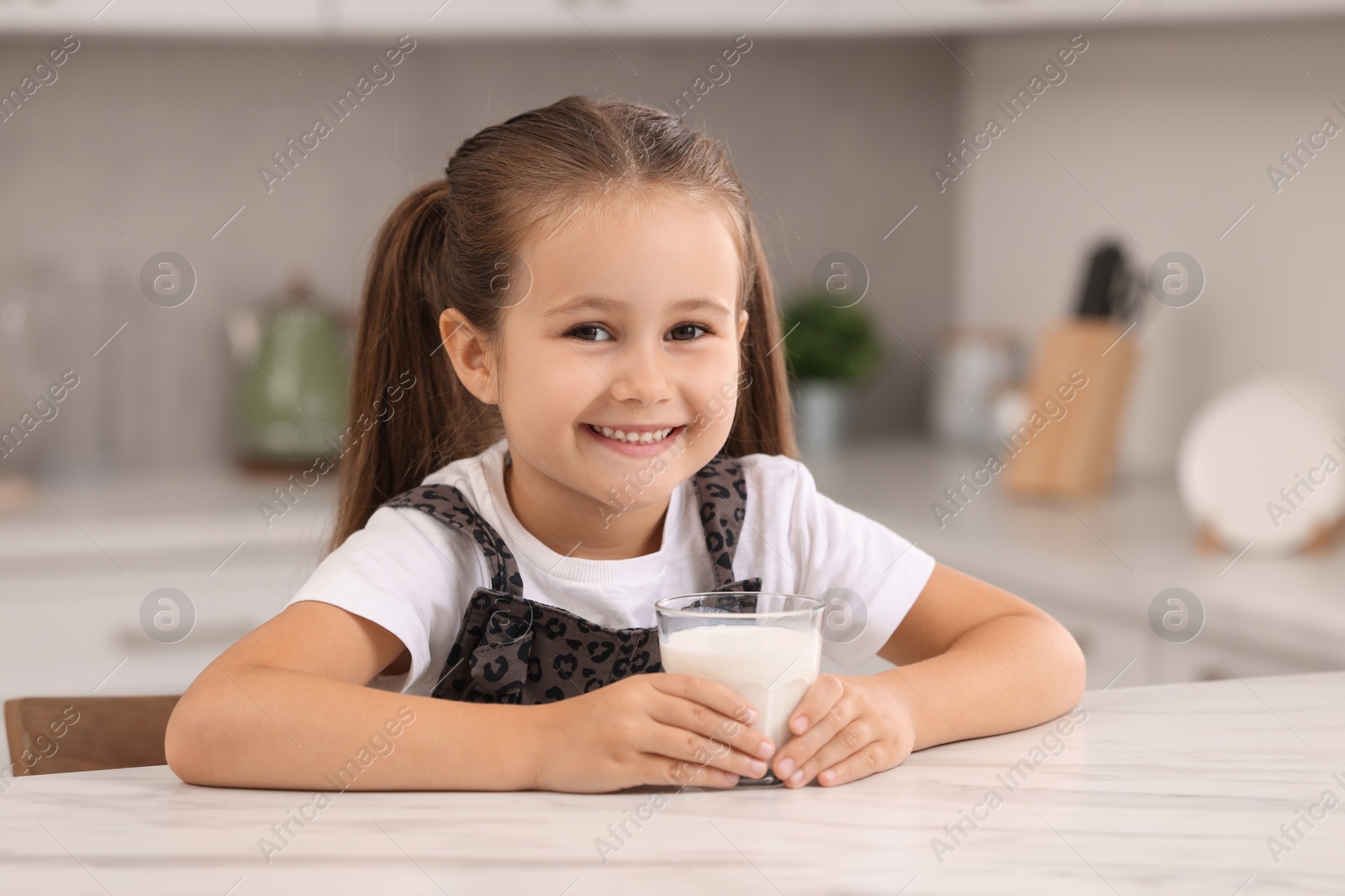 Photo of Cute girl with glass of milk at white table in kitchen