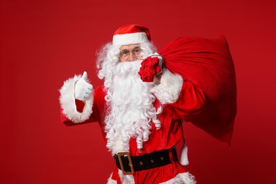 Photo of Santa Claus with bag of Christmas presents showing thumbs up on red background