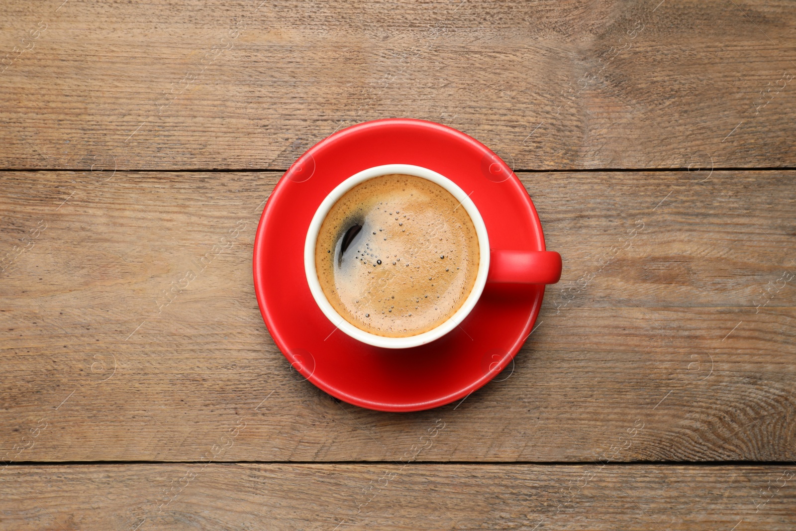 Photo of Aromatic coffee in red cup on wooden background, top view