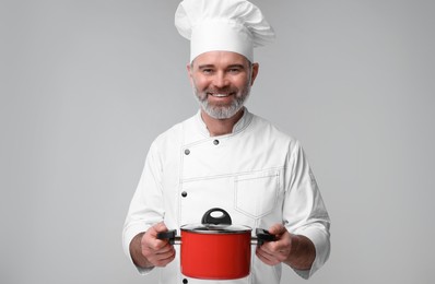 Photo of Happy chef in uniform with cooking pot on grey background