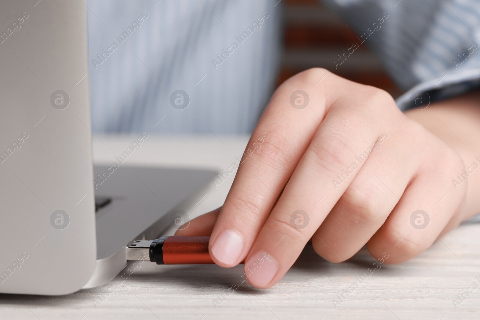 Photo of Woman attaching usb flash drive into laptop at wooden table, closeup