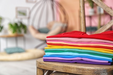 Photo of Stack of colorful t-shirts on chair in living room